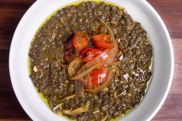 Overhead shot of a bowl of chicken and lentil stew topped with fried onions and tomatoes