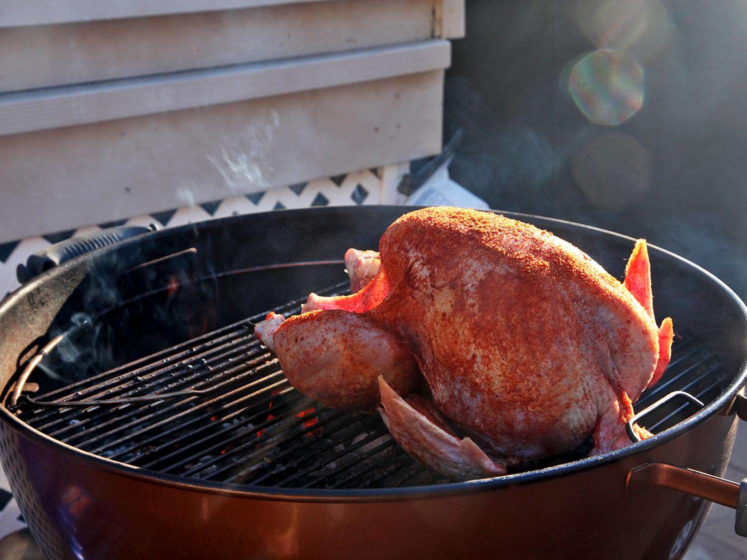 Whole, rubbed turkey placed on the grate of a kettle grill, ready to be smoked.