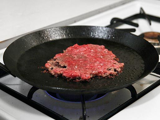 Fully smashed hamburger patty on a smoking hot carbon steel skillet.