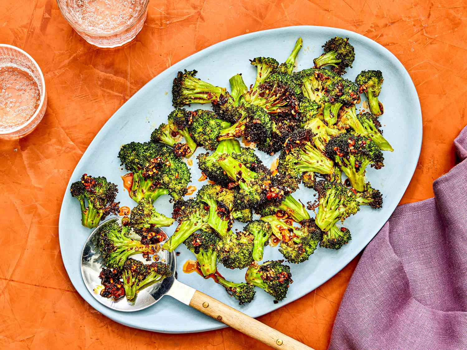 Air-fried broccoli with chili crisp on a blue platter against an orange background.