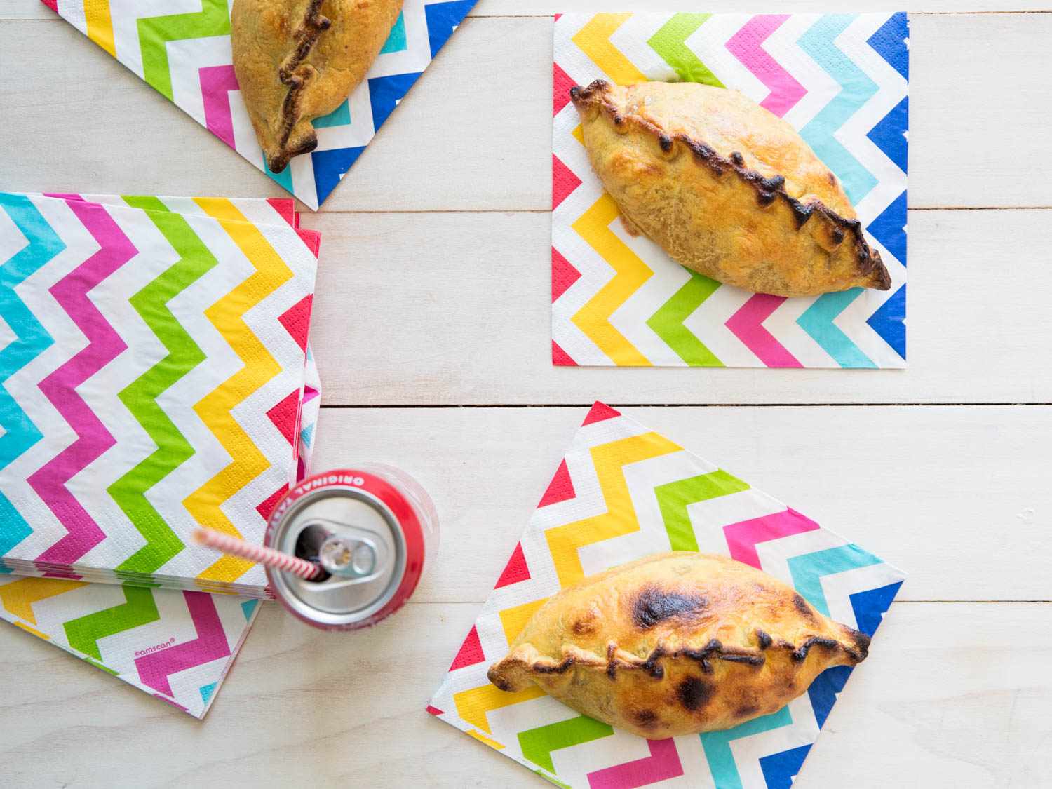 The finished salteñas, served on colorful napkins with a can of cola.