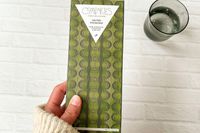 A hand holding Compartés Salted Pistachio Chocolate Bar next to a glass