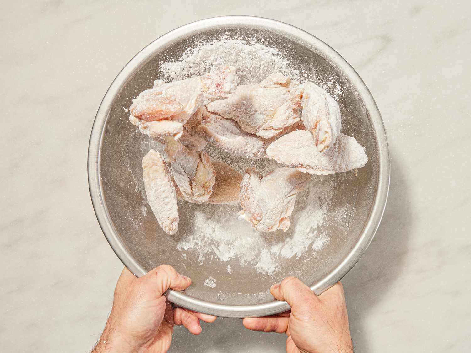 Overhead view of tossing wings in flour