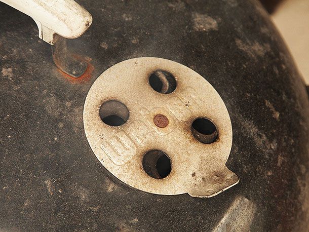 Close-up of the top vent of a kettle-style grill. The vent is partially closed.
