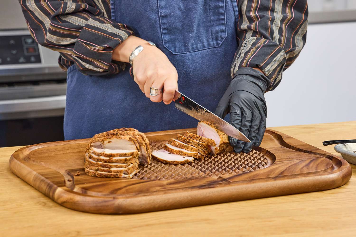 Person slicing roasted meat on a Lipper International Acacia Cutting Board with Grid Grip