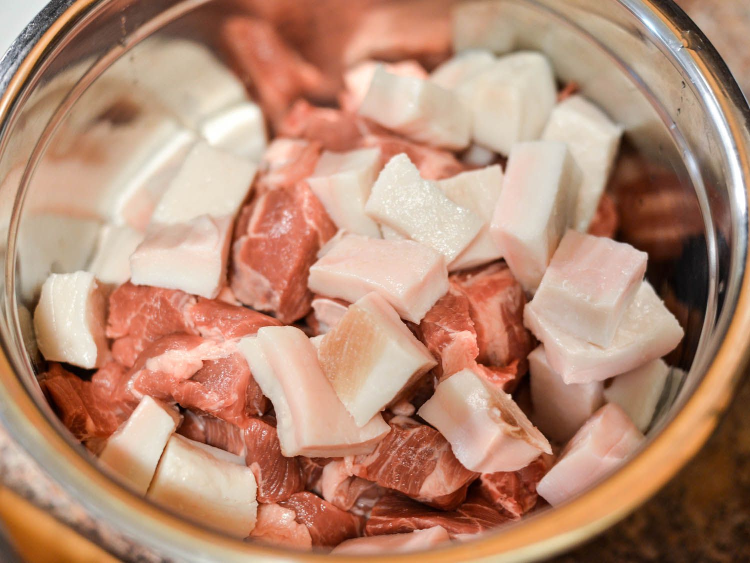 Chunks of fatback, lamb, and pork in a mixing bowl, ready to be ground.
