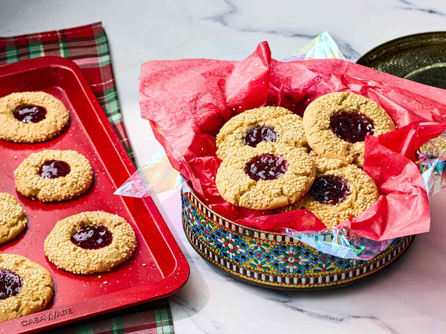 Thumbprint cookies with jam displayed on a decorative tin and on a baking tray