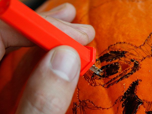 Using a toothed pumpkin-carving tool to cut small holes in a photographic design on a pumpkin