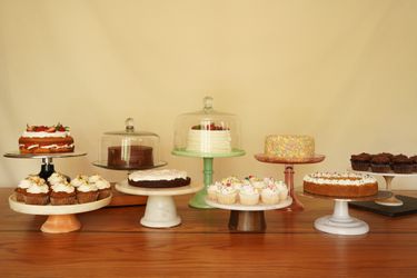 Nine cake stands holding cakes and cupcakes sit on a wooden surface