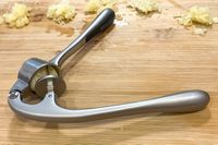 A garlic press with crushed garlic on a cutting board