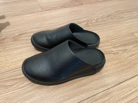 A pair of black Snibbs clogs on a wooden floor.