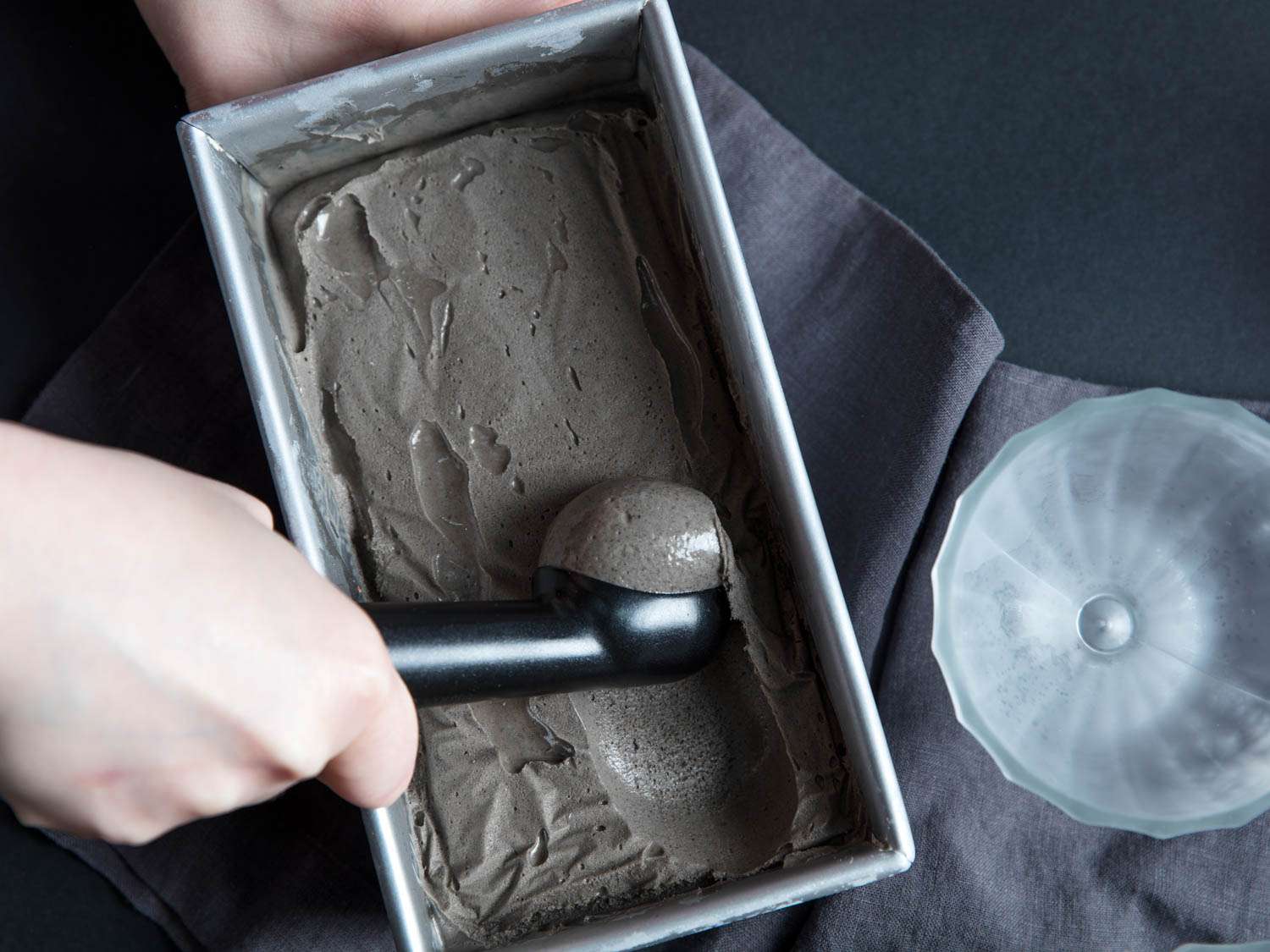 Scooping out black sesame ice cream from a frozen loaf pan.