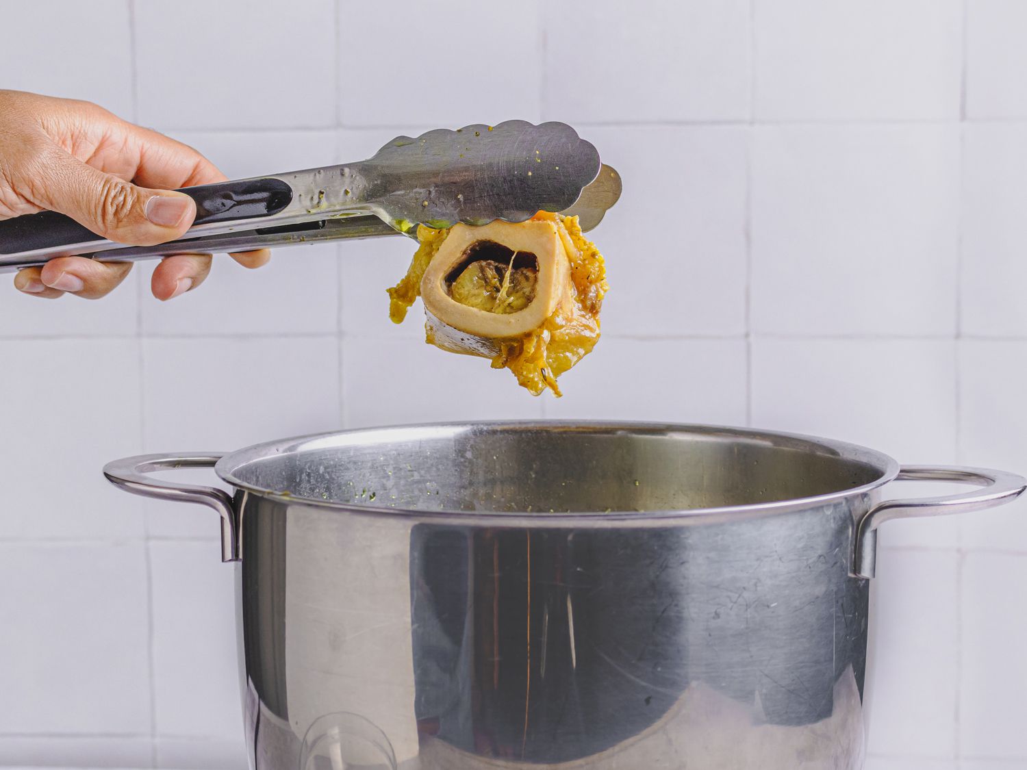 A pair of thongs lifting a bone from the broth