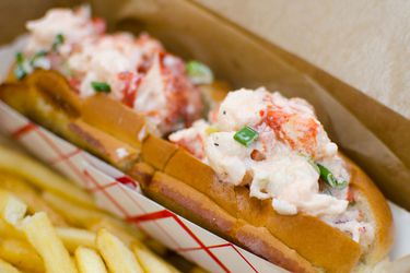 Lobster rolls in a basket next to some French fries. 