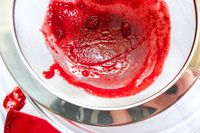 Rösle Stainless Steel Round Handle Kitchen Strainer containing strained red puree or sauce over a bowl