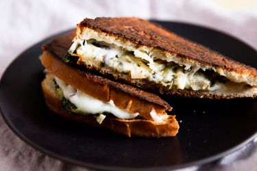 Closeup of a halved and shingled Spinach and Artichoke Grilled Cheese Sandwich, served on a black plate.