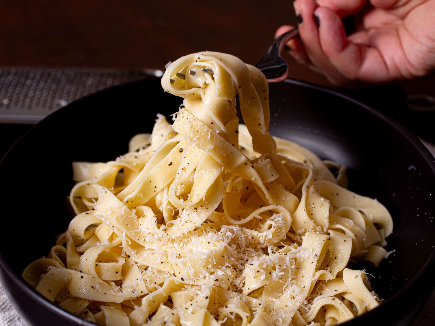 A plate of pasta being twirled on a fork topped with grated cheese and seasoning