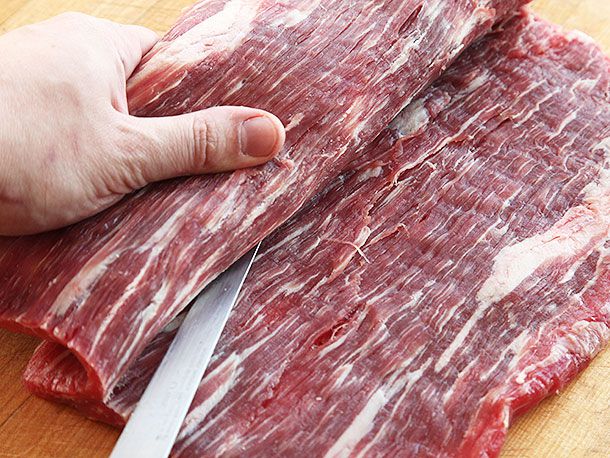 Large piece of raw flank steak being butterflied into one large square