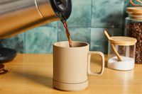 Pouring coffee into a tan ceramic mug.