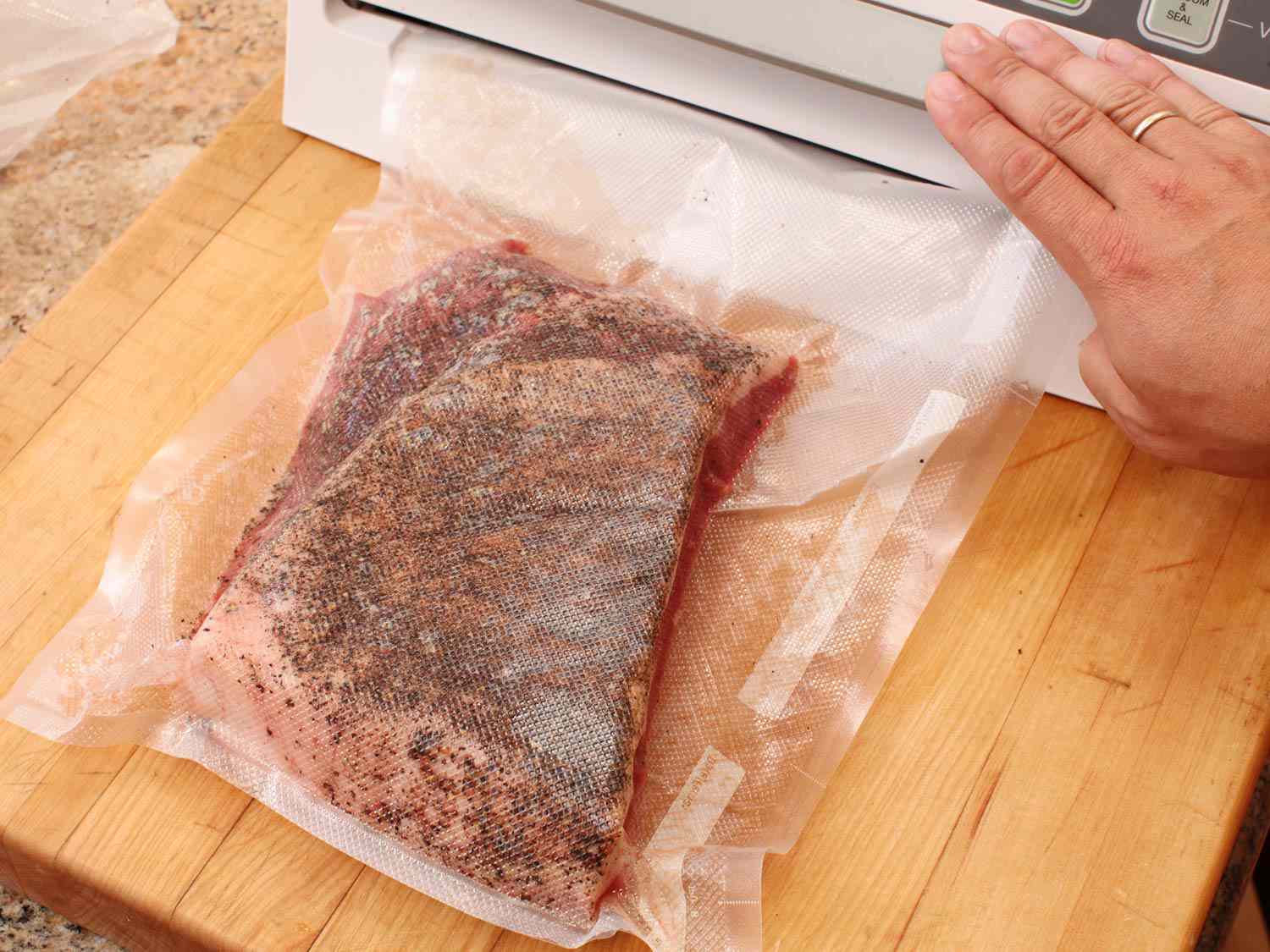 Sealing half a peppercorn-crusted brisket in a vacuum bag
