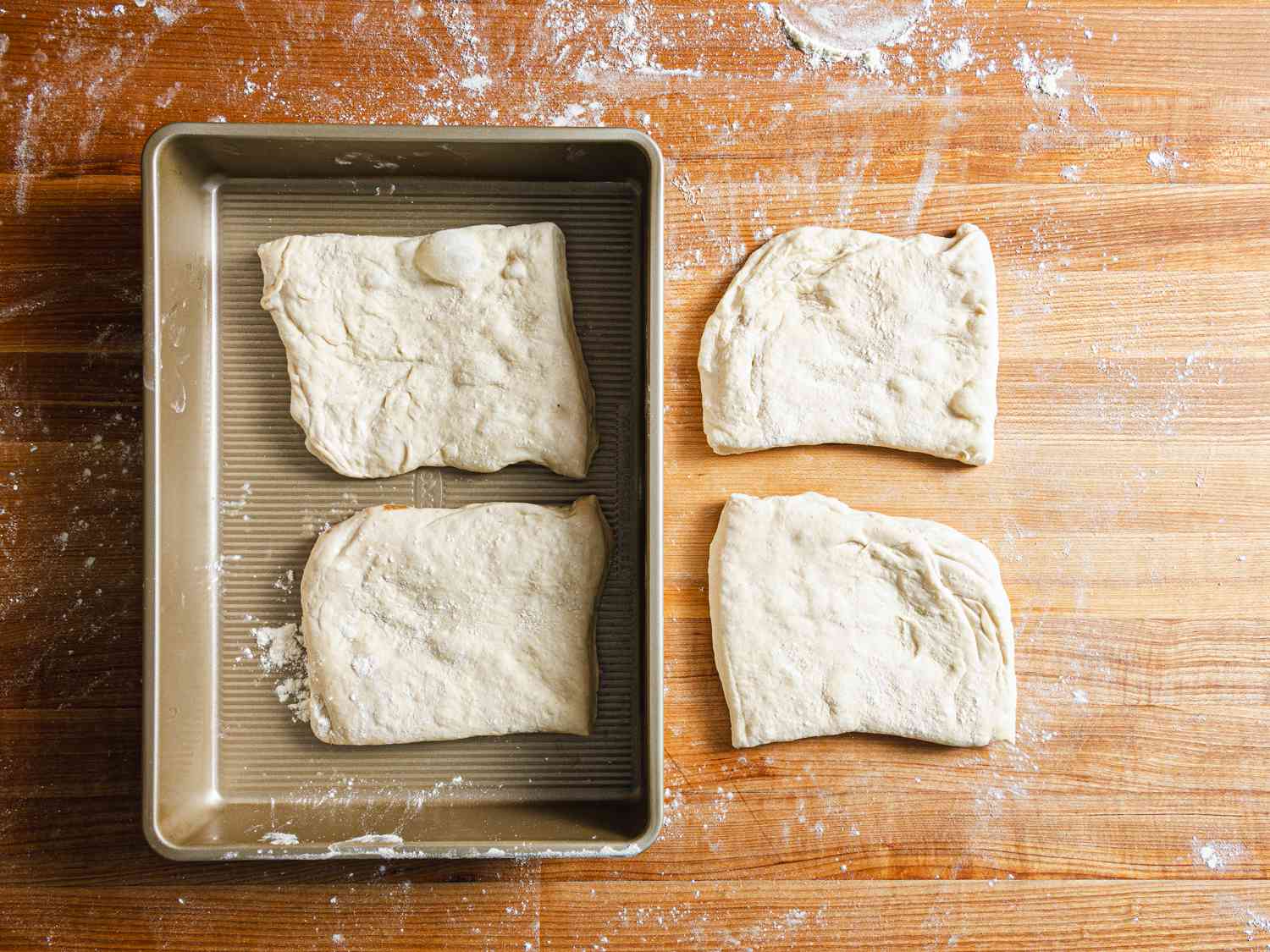 Dough separated into four sections, two in a pan, two on a floured surface 