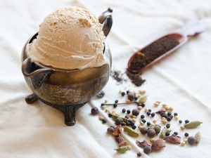 A scoop of chai flavored ice cream in a small teapot, alongside whole spices.
