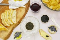 A spread on a table featuring bread slices caviar tins with a bowl of ice chips and a glass of wine