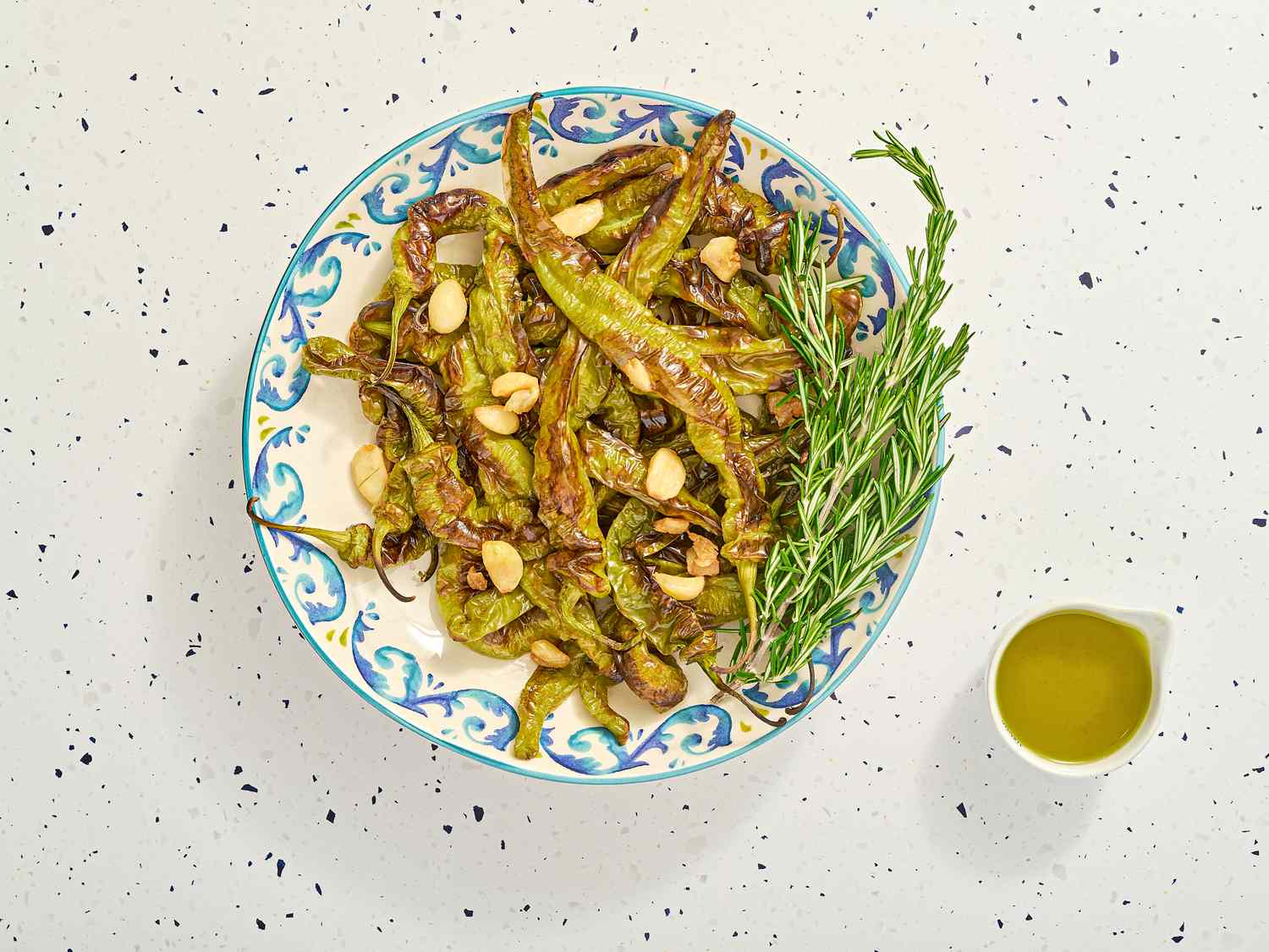 A plate of roasted green beans topped with almonds and rosemary next to a small container of olive oil