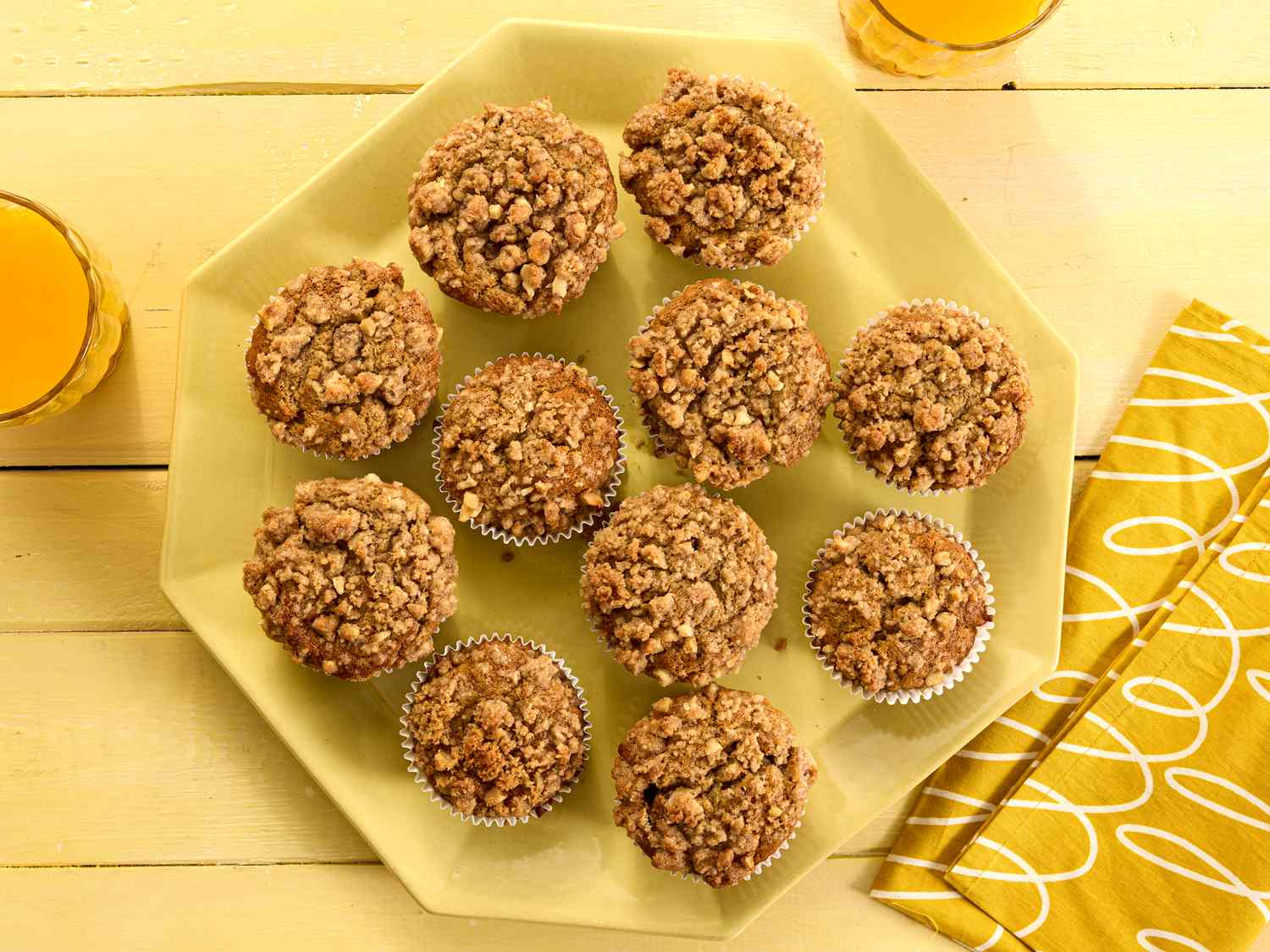 banana nut muffins on a yellow platter, with yellow napkins, a yellow tabletop and orange juice 