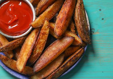 Closeup of a serving plate of roasted potato wedges with a ramekin of ketchup.