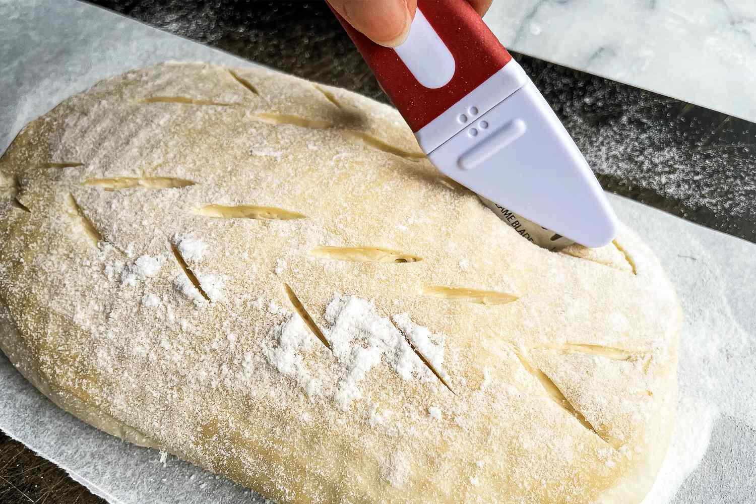 A person using the Breadsmart bread lame to score a design in a loaf of bread