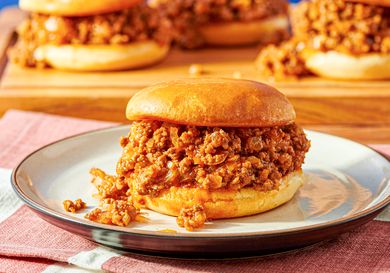 A sloppy joe served on a plate with more sandwiches in the background