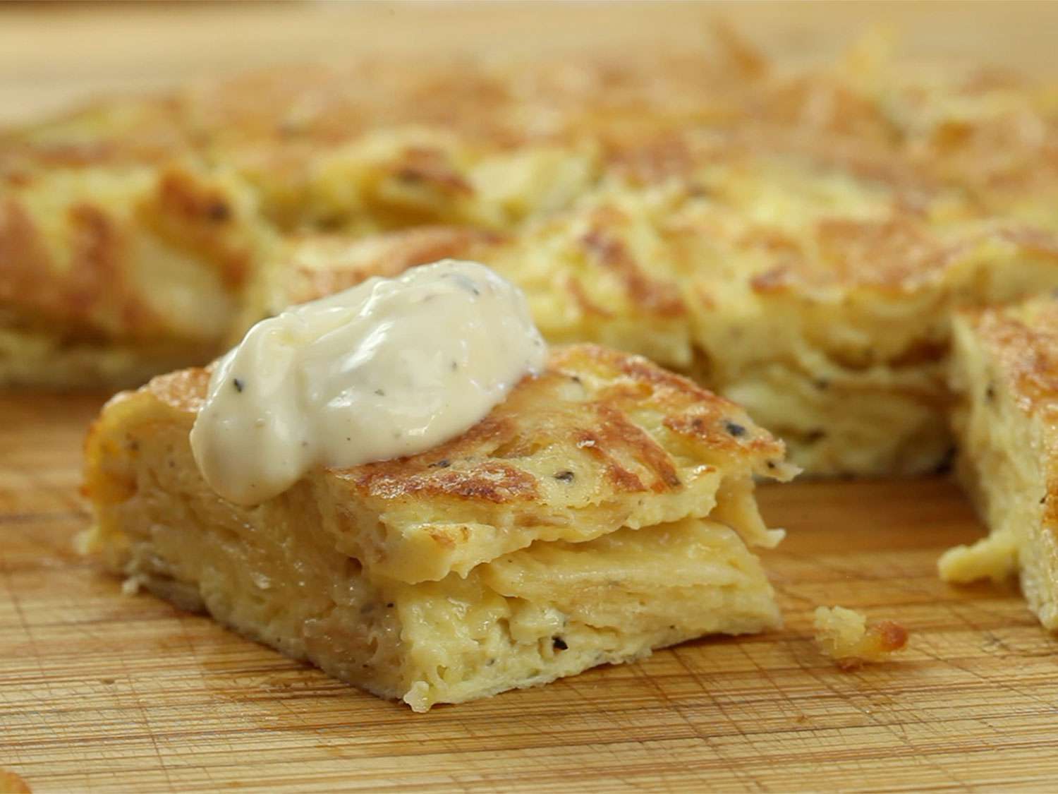 A slice of salt-and-vinegar Spanish tortilla resting on a cutting board, topped with quick cheaty allioli.