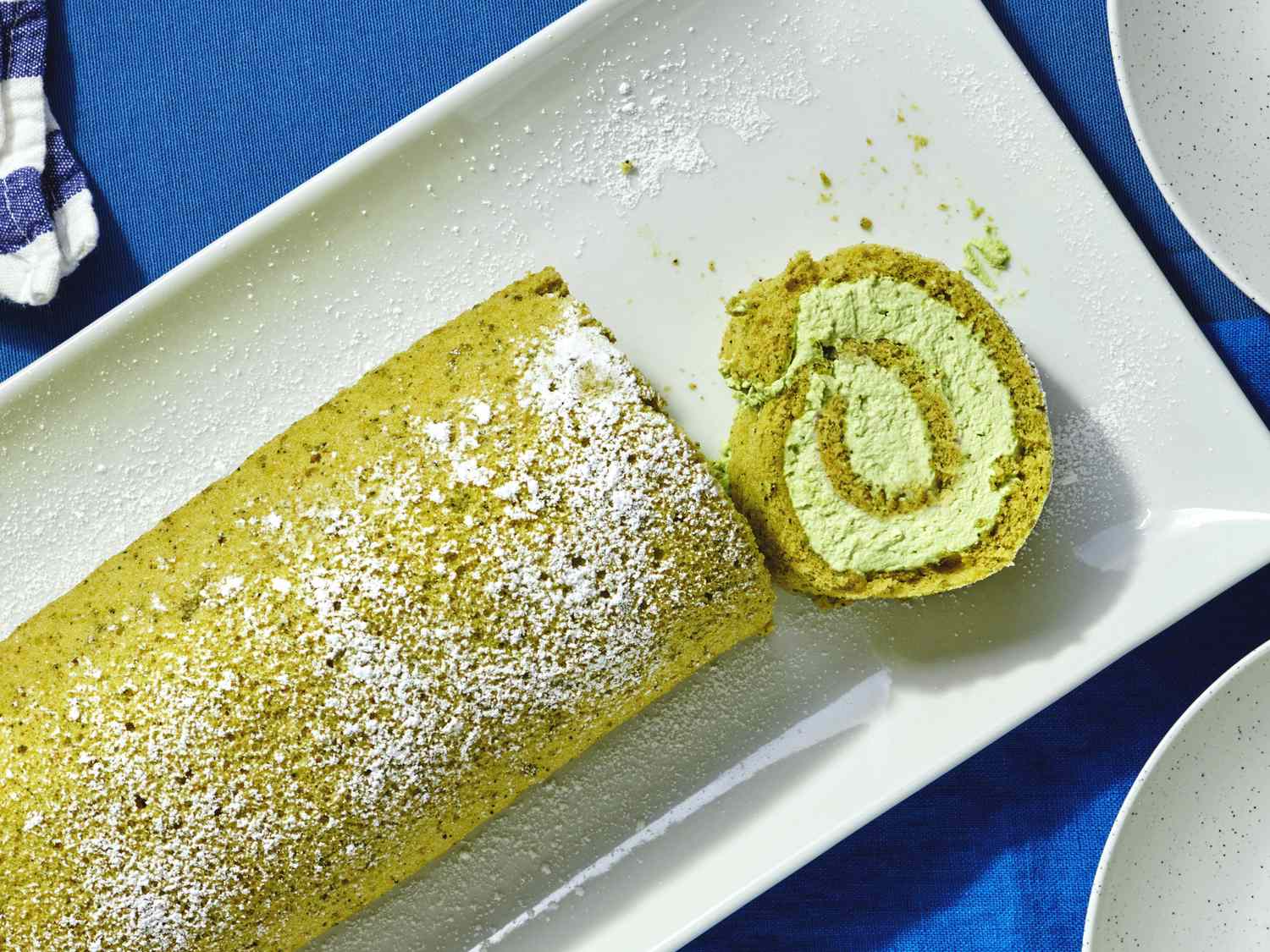 Matcha Swiss roll on a white plate partially sliced