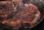 Two dry-aged steaks cooking in a cast iron skillet. 