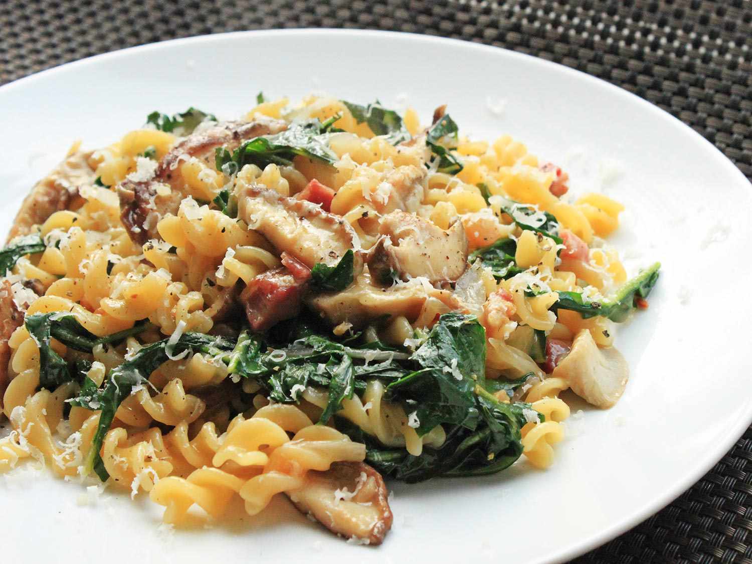 Slide view of a plate of pasta tossed with browned pancetta, mushrooms, and wilted greens.