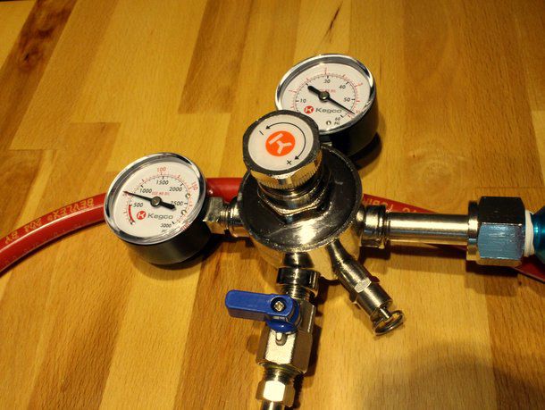 The regulator value placed on a wood floor. There is a red rubber hose behind the valve.