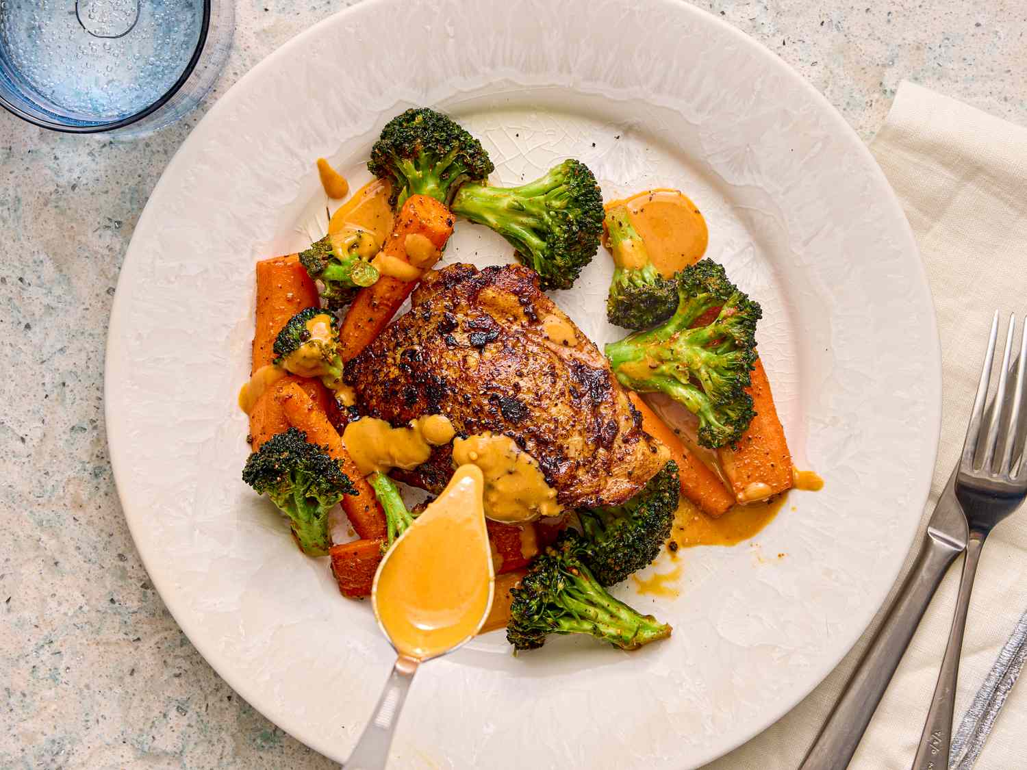 A plate with roasted chicken broccoli and carrots with a drizzle of sauce