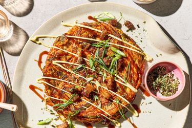 A plated carrot okonomiyaki topped with garnishes and sauces, viewed from above