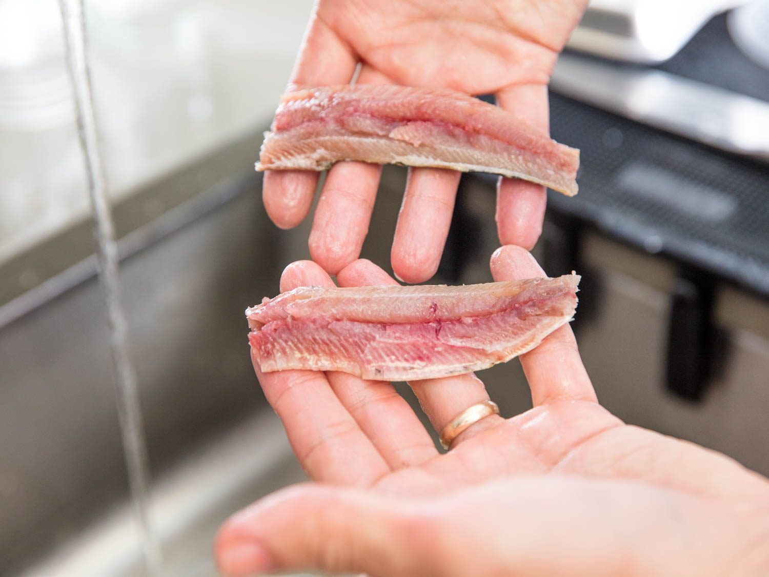 Hands holding two halves of a separated fresh sardine fillet.