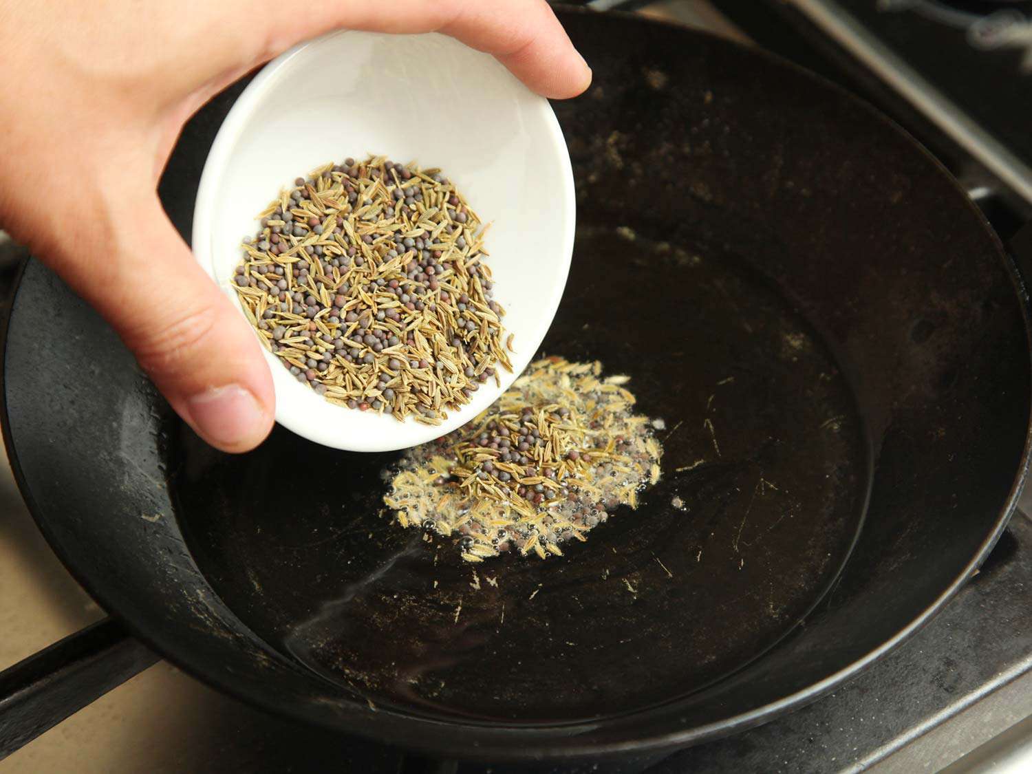 Putting cumin and mustard seeds into hot oiled skillet to toast