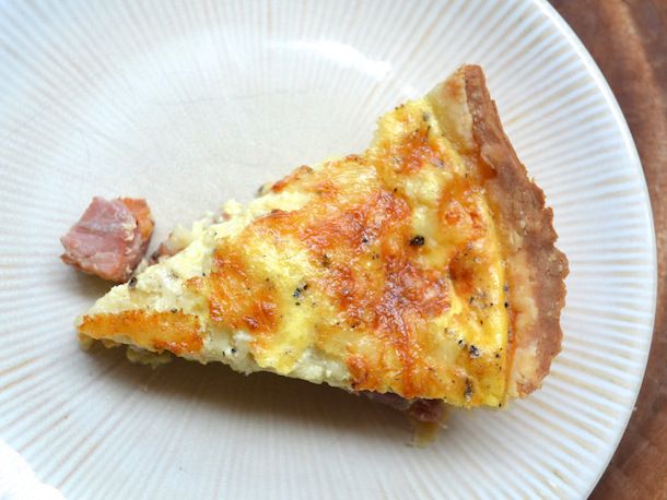 Overhead view of a slice of ham and cheese quiche served on a white plate.