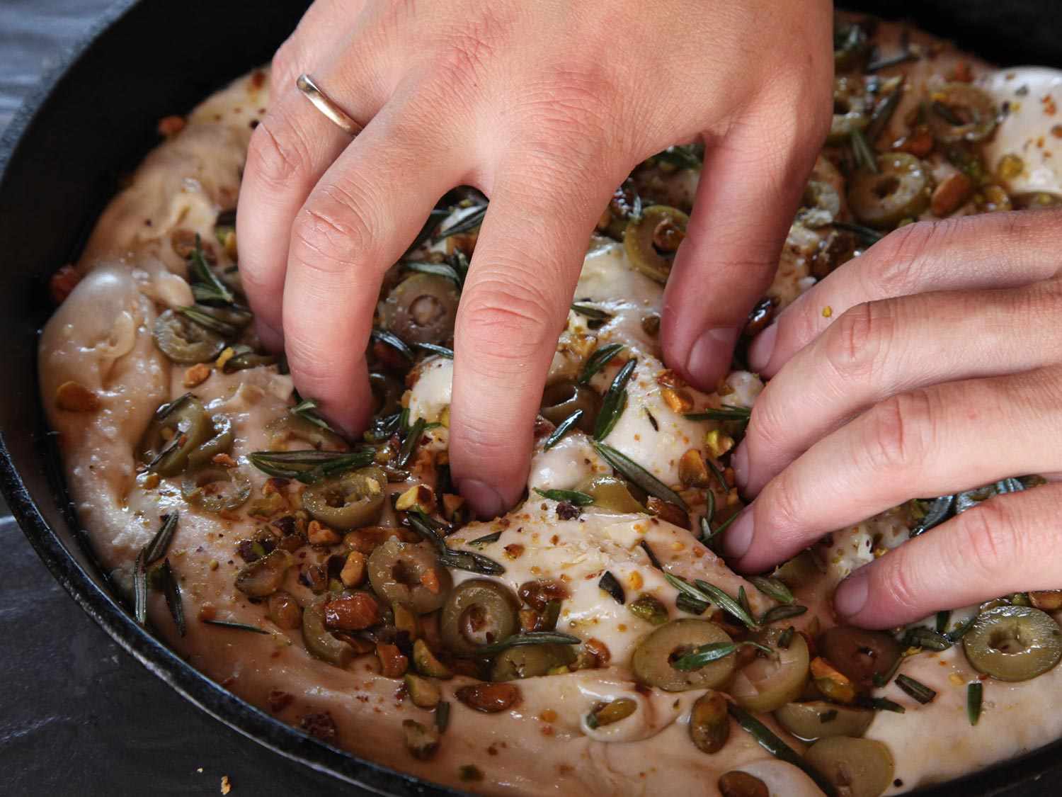 Pressing olives and pistachios into focaccia dough with fingertips