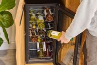 A hand placing a wine bottle into a wine cooler with multiple bottles