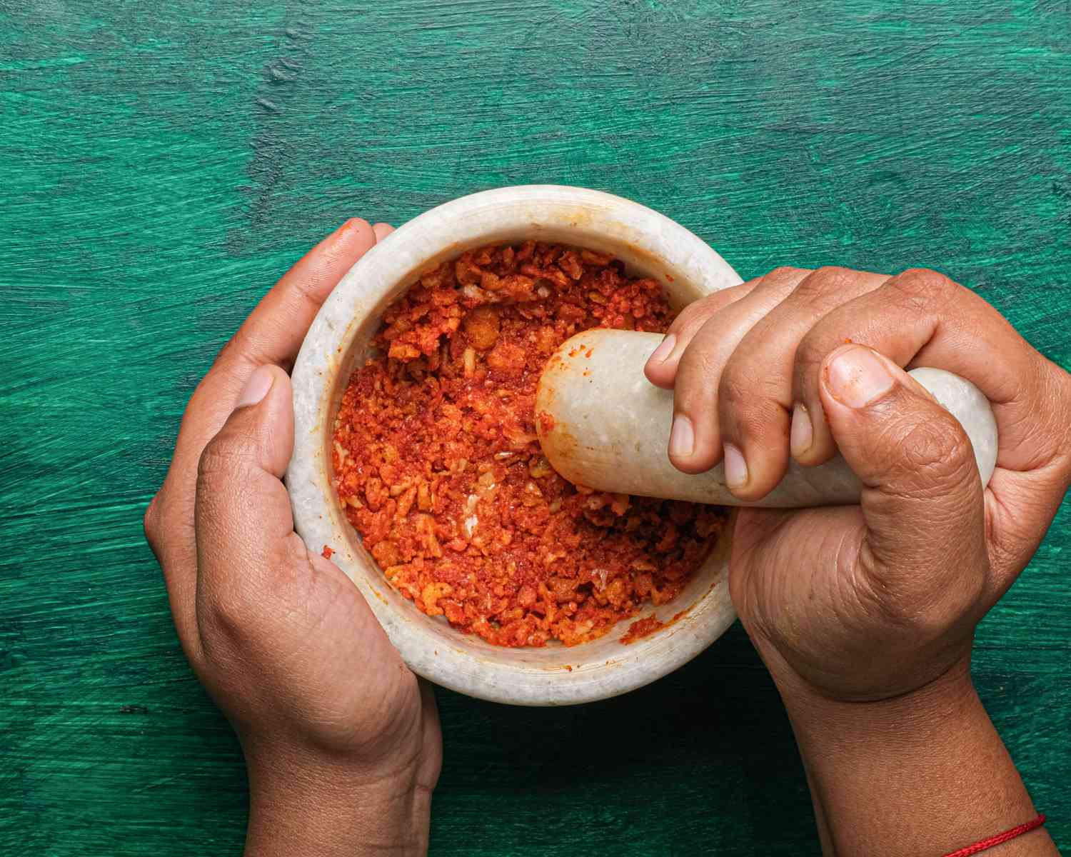 Pounding garlic and breadcrumbs with a mortar and pestle.