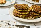 A plate of fritters stacked on a floralpatterned dish served with a side of yogurt sauce and a knife