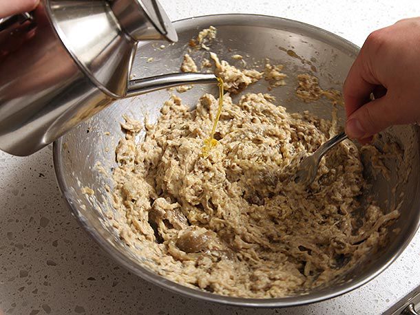 Adding olive oil in a thin stream to a metal bowl of mashed eggplant