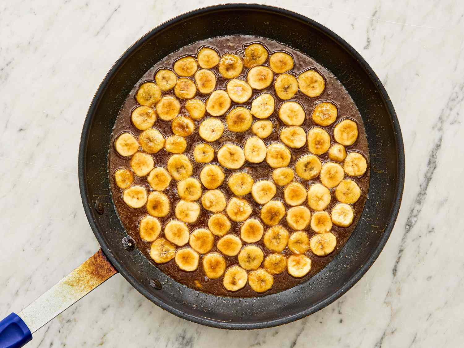 Sauted banana slices in a pan arranged in a circular pattern on a light marble surface possibly a dessert preparation step