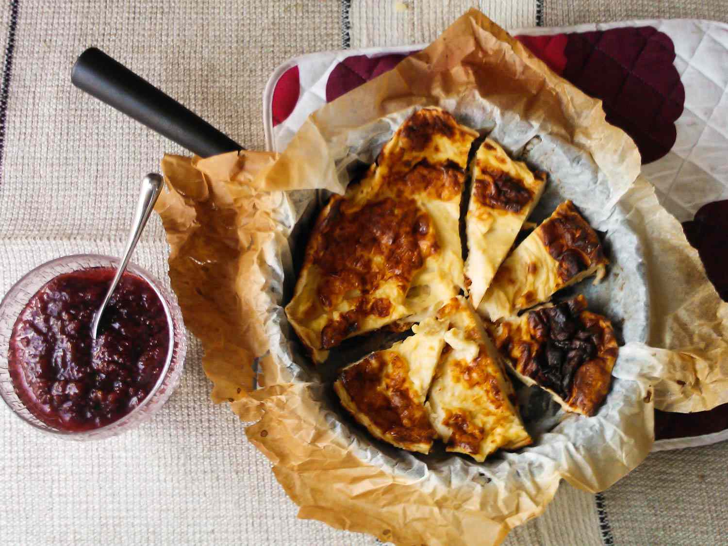 A large pannukakku in parchment paper on a skillet, with a bowl of jam next to it.
