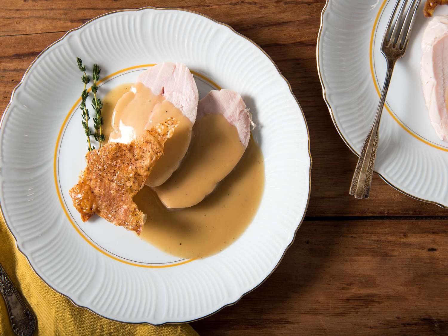 Overheasd view of several slices of sous vide turkey breast, smothered in gravy and topped with crispy skin.